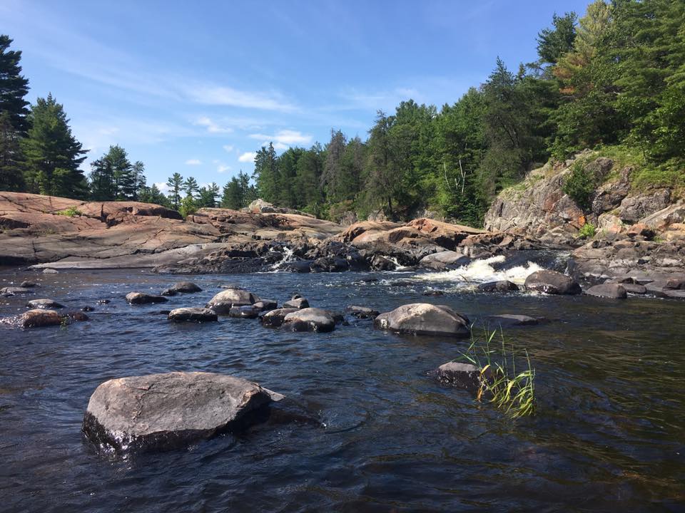 Scenery photo displaying the upper end of the Sturgeon Chutes in the Northern part of the Lower French River Provincial Park, Northeastern Ontario Canada. The image displays rocky granite structure, green vegetation, Pine trees, and a small waterfall.