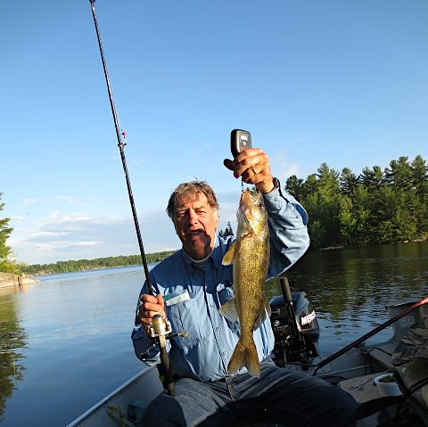 Image of a man holding a Walleye and his Fishing Rod and Spinning Reel while jigging in the French River, Ontario.